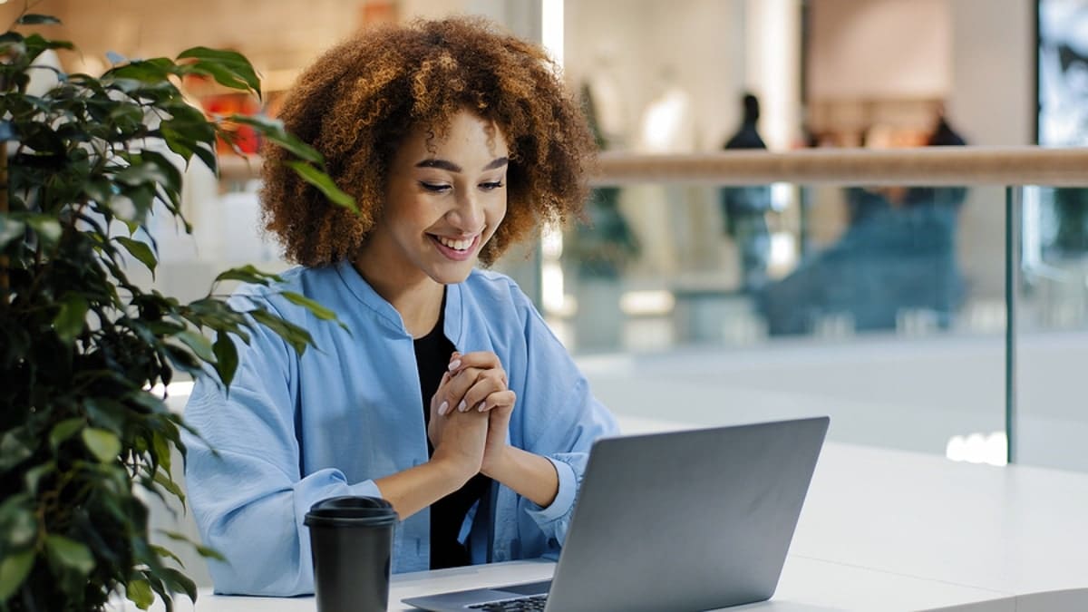 African american girl student using laptop while sitting at a desk and drinking coffee