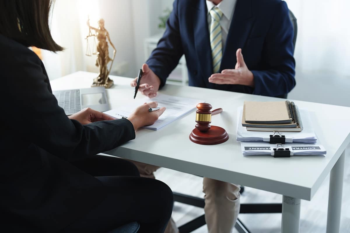 attorney and client sitting at a table with a gavel and pile of paperwork