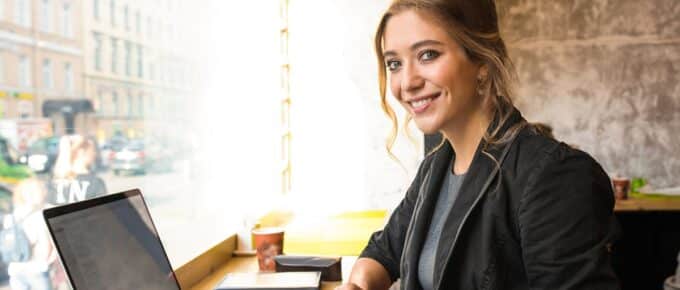 Smiling woman professional government worker looking in camera while sitting in coffee shop with laptop computer during coffee break