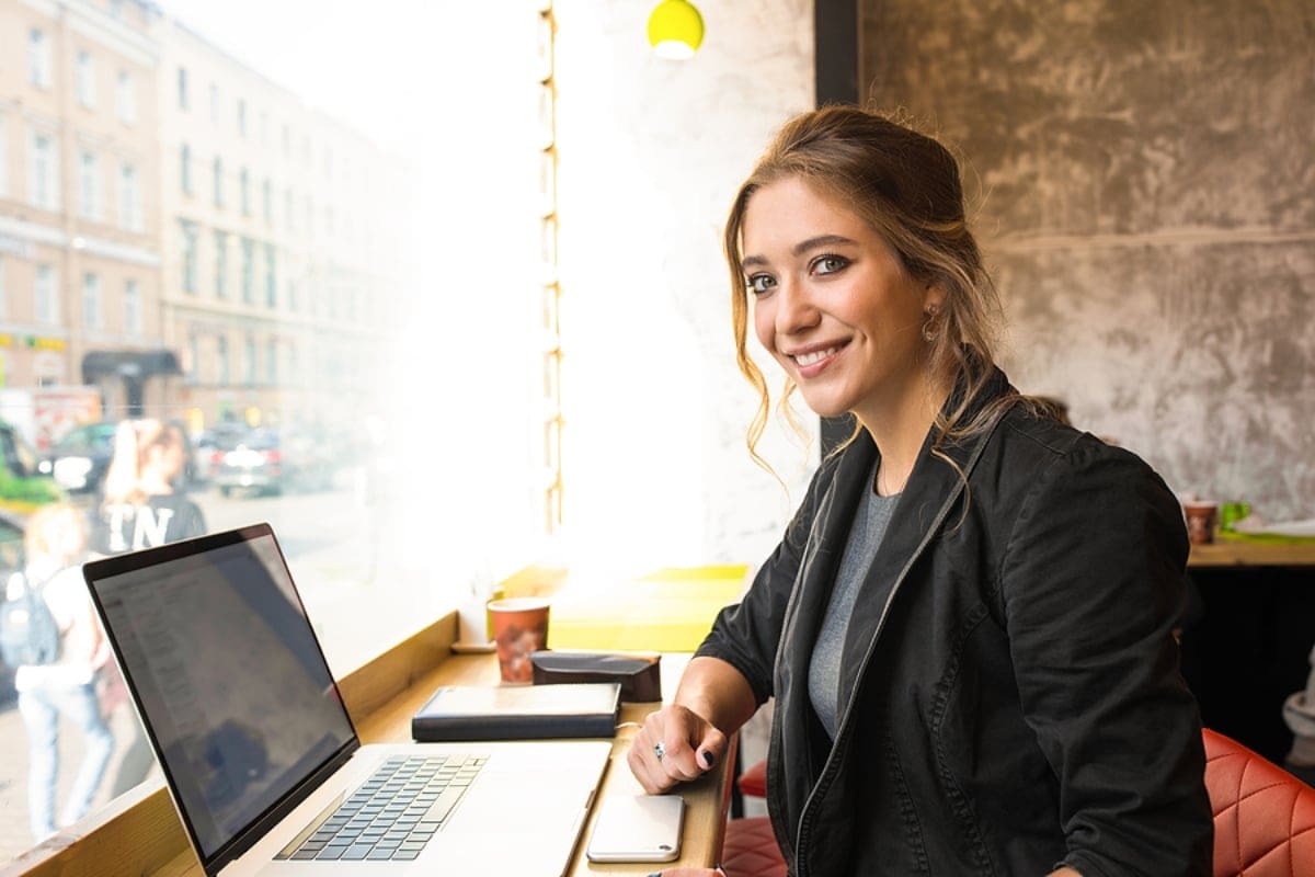 Smiling woman professional government worker looking in camera while sitting in coffee shop with laptop computer during coffee break