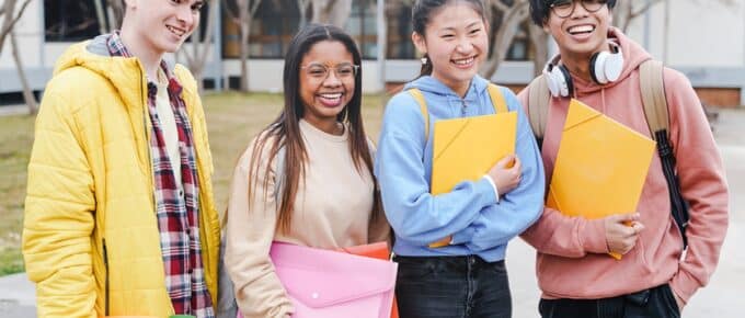 Group of multicultural students standing in front of a college, each holding folders.