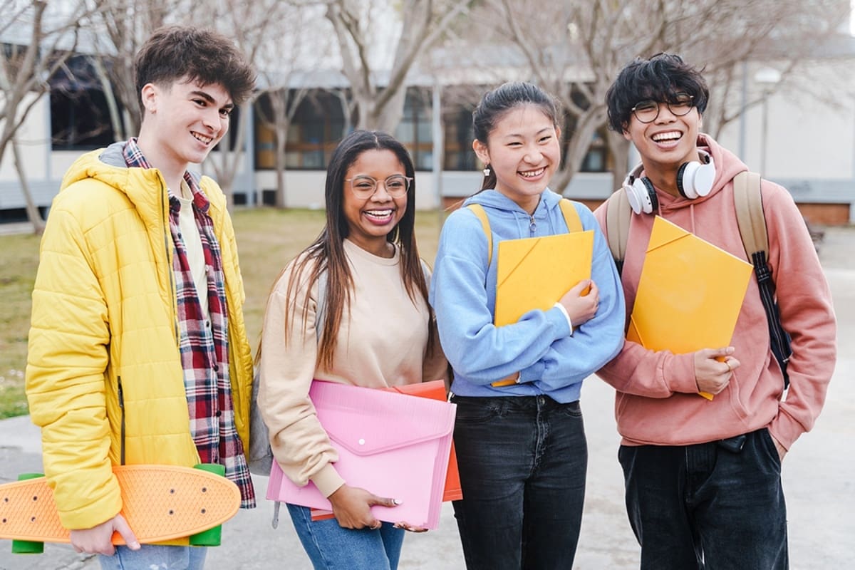 Group of multicultural students standing in front of a college, each holding folders.