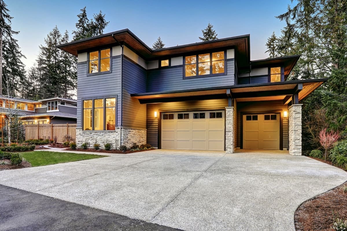 Luxurious new construction home with two car garage framed by blue siding and natural stone wall trim