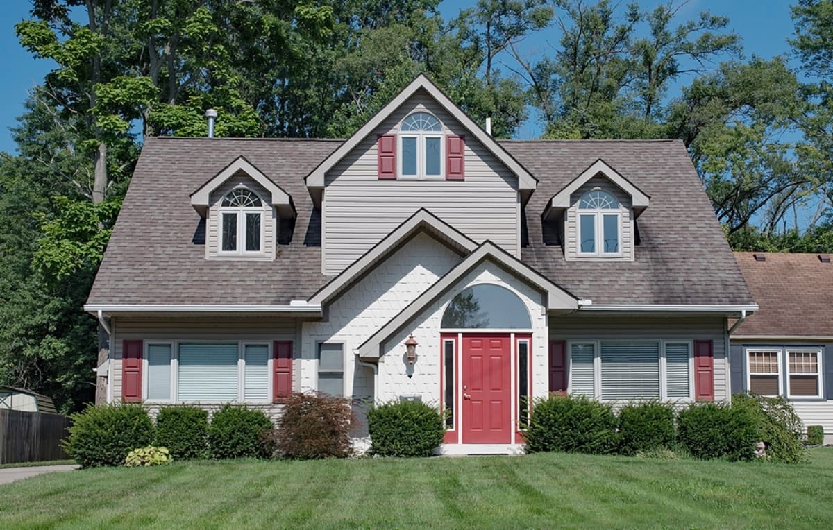 Gray House with Red shutters and a red door with lush green lawn