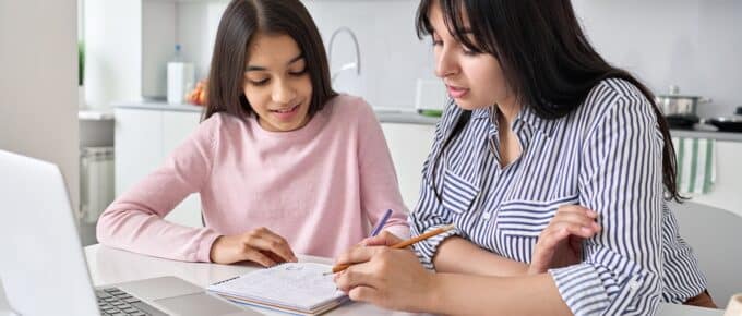 Young indian mother helping teen daughter with college application and financial aid sitting at a desk with a laptop computer.