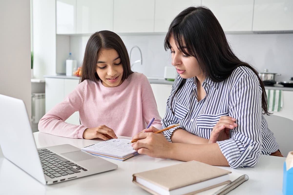 Young indian mother helping teen daughter with college application and financial aid sitting at a desk with a laptop computer.