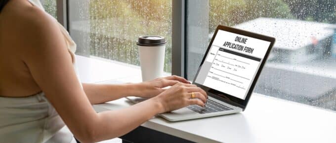 woman with long dark hair wearing a white shirt filling out FAFSA online while sitting in a cafe