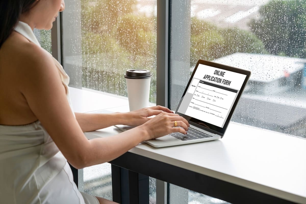 woman with long dark hair wearing a white shirt filling out FAFSA online while sitting in a cafe