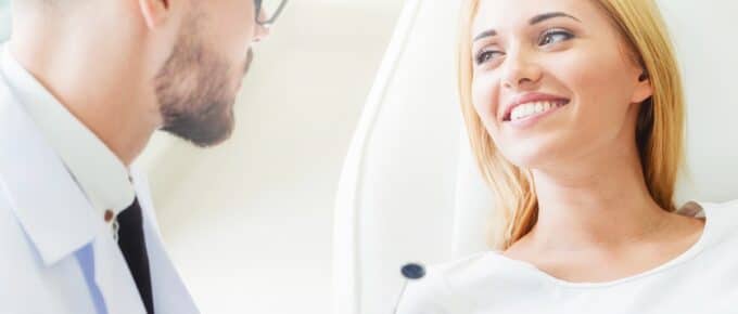 Young dentist examining teeth of happy woman patient sitting on dentist chair in dental clinic.