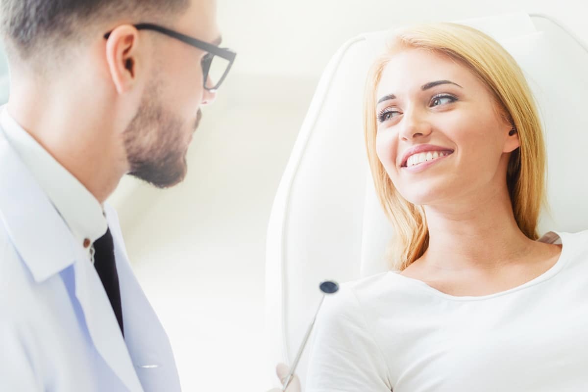 Young dentist examining teeth of happy woman patient sitting on dentist chair in dental clinic.