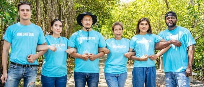 six volunteers wearing blue t-shirts that say volunteer standing, linking arms, surrounded by trees.