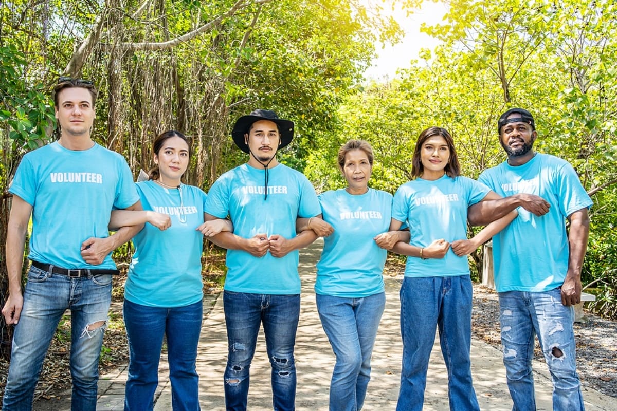 six volunteers wearing blue t-shirts that say volunteer standing, linking arms, surrounded by trees.