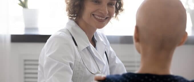 Happy young female oncologist supporting bald woman.
