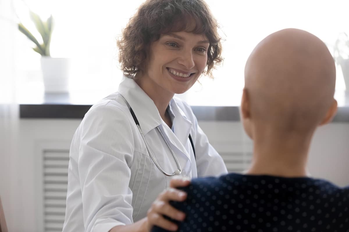 Happy young female oncologist supporting bald woman.