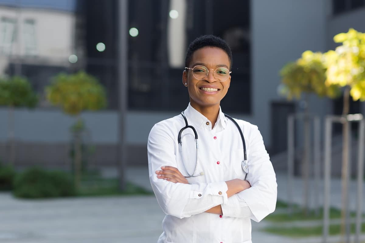 Portrait of female doctor happy successful smiling and looking at camera near clinic in medical gown
