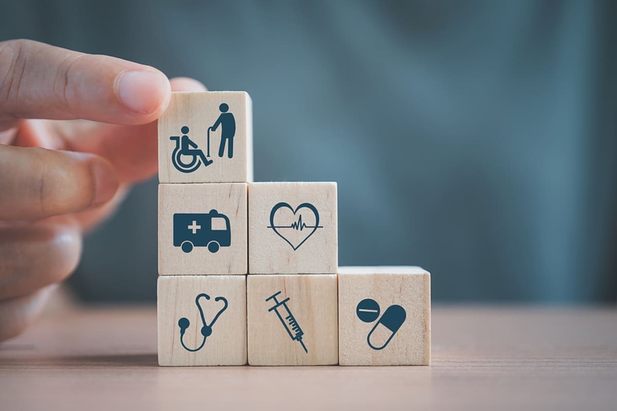 adult hand holding wooden cube block with image of wheel chair, health and medical symbol for health insurance and other medical symbols.