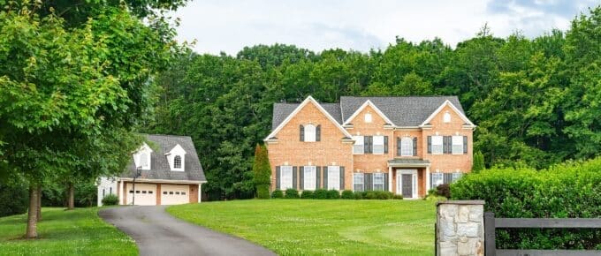 Large 2-story brick home in the country with green grass, a long driveway, and blue sky.