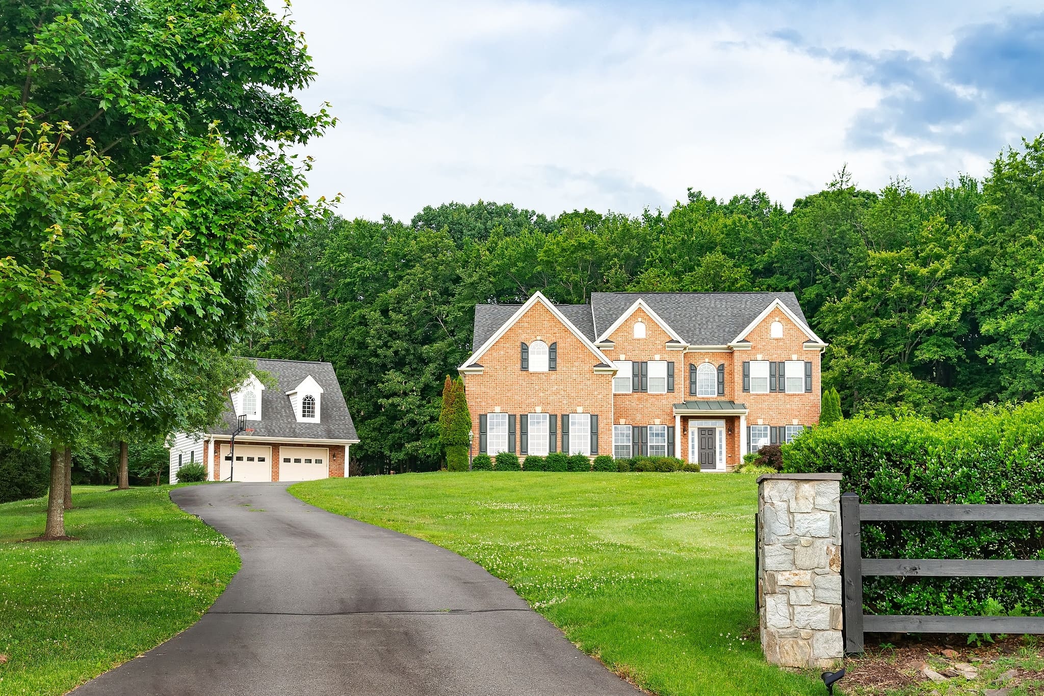 Large 2-story brick home in the country with green grass, a long driveway, and blue sky.