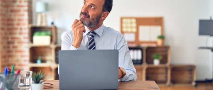 Middle age handsome businessman wearing tie sitting using laptop at the office with hand on chin thinking about question