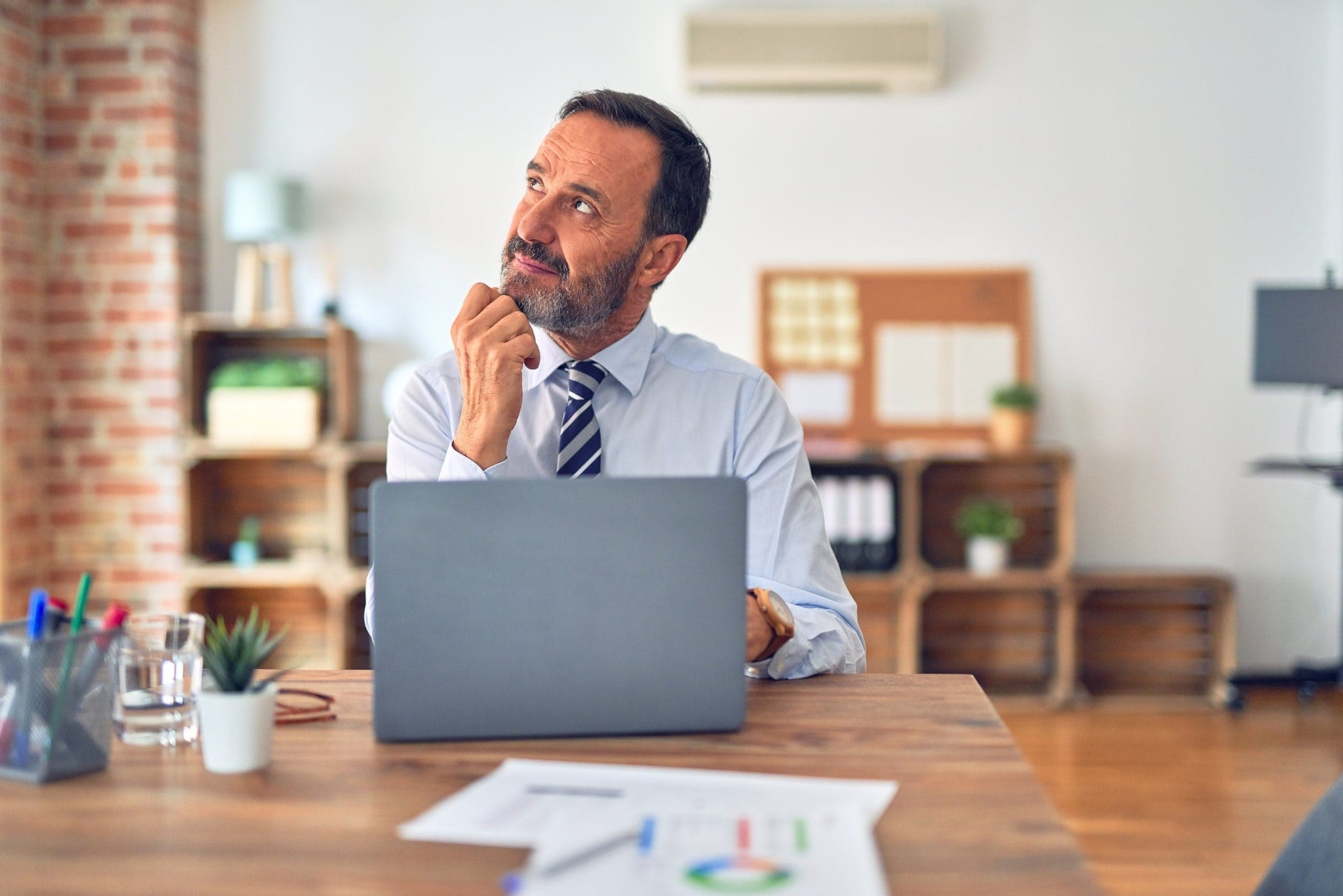 Middle age handsome businessman wearing tie sitting using laptop at the office with hand on chin thinking about question