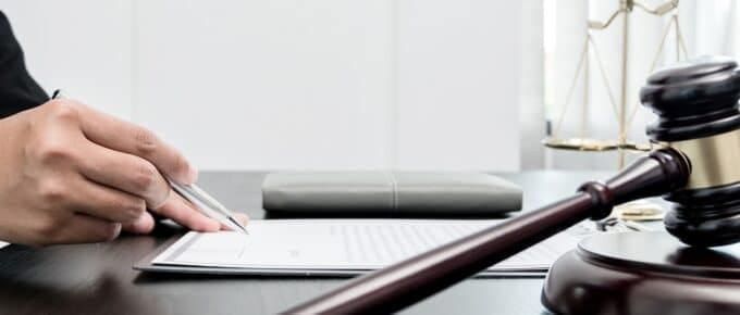 A woman's hand holds a pen, preparing to sign a document on a desk with a judge's gavel
