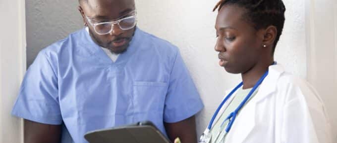 african american doctor and nurse standing looking at a clipboard.