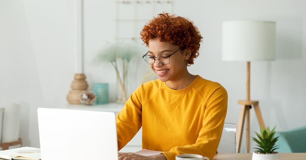 African american girl using laptop at home office looking at screen typing