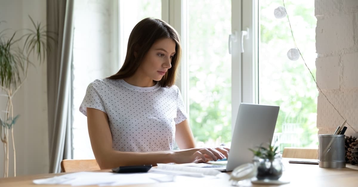 Focused young woman checking financial documents, using laptop