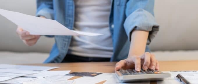 Asian young woman holding papers and typing into calculator