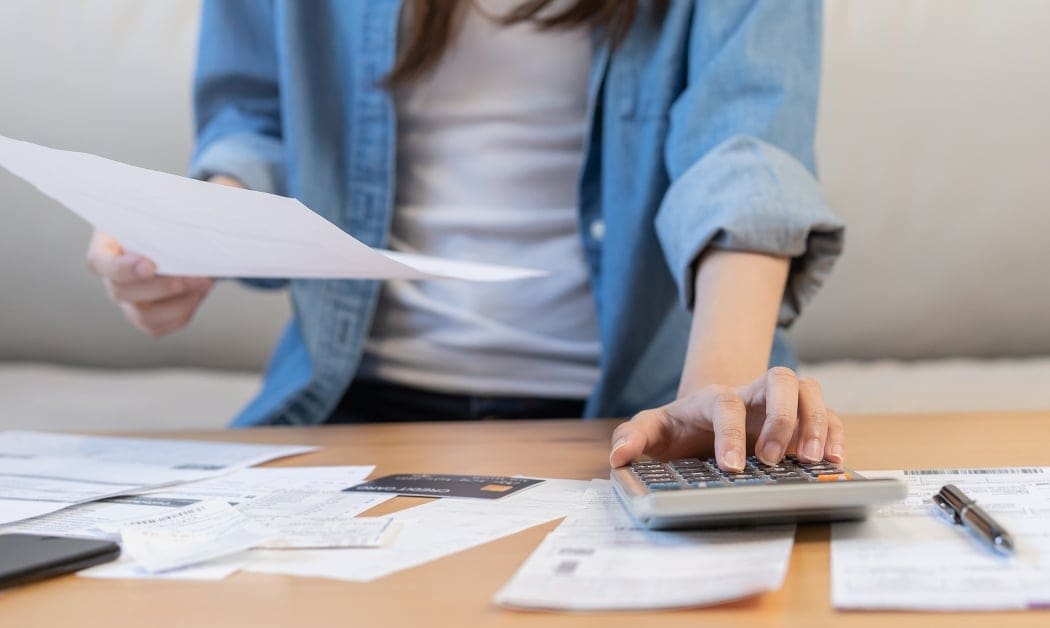 Asian young woman holding papers and typing into calculator