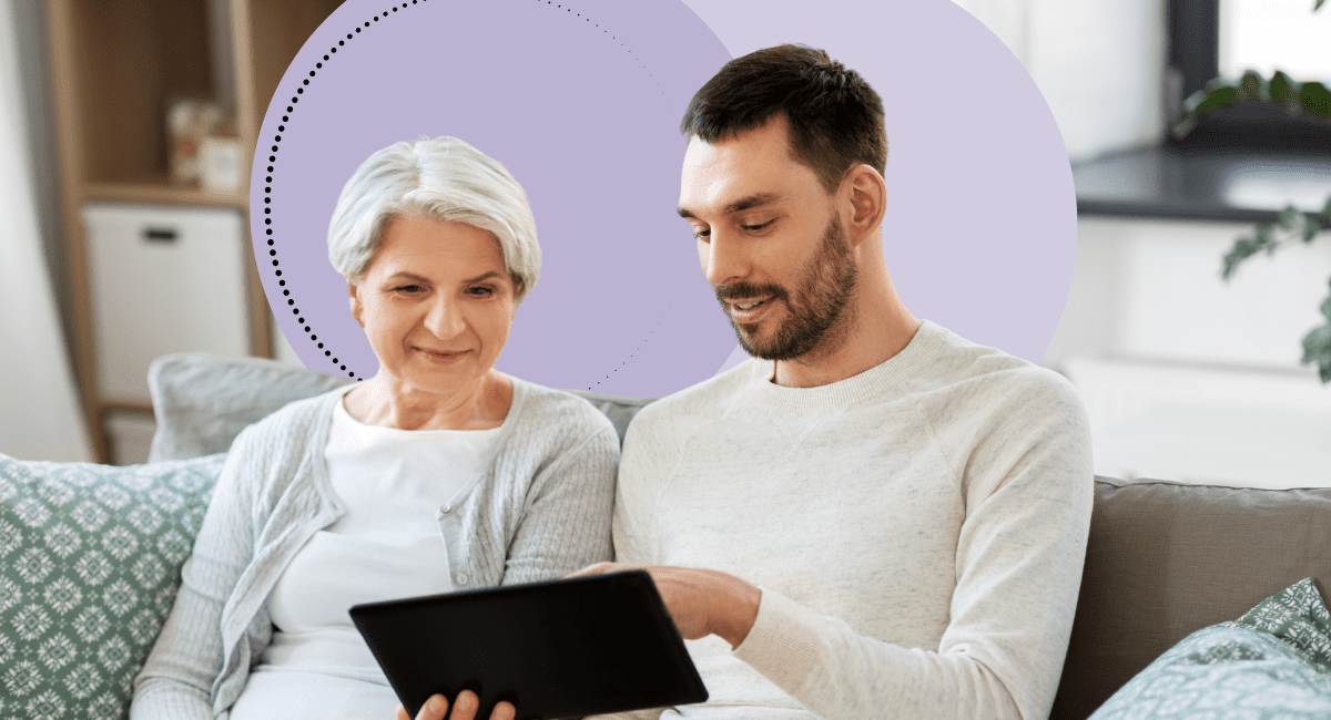 A man and elderly woman sitting on a couch looking at an ipad.