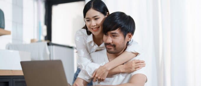 Young married couple showing happy smiling faces and using computers and notebooks to calculate household income and expenses