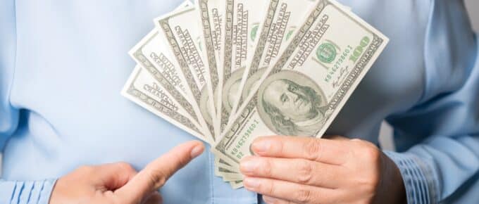 Portrait of successful happy woman with fancy brown hair pointing to dollar bills
