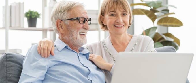 Man and woman using laptop computer on sofa at home together.