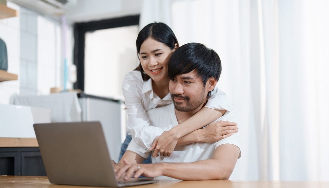 Young married couple showing happy smiling faces and using computers and notebooks to calculate household income and expenses