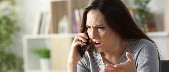 Angry woman calling arguing on smart phone sitting in the living room at home
