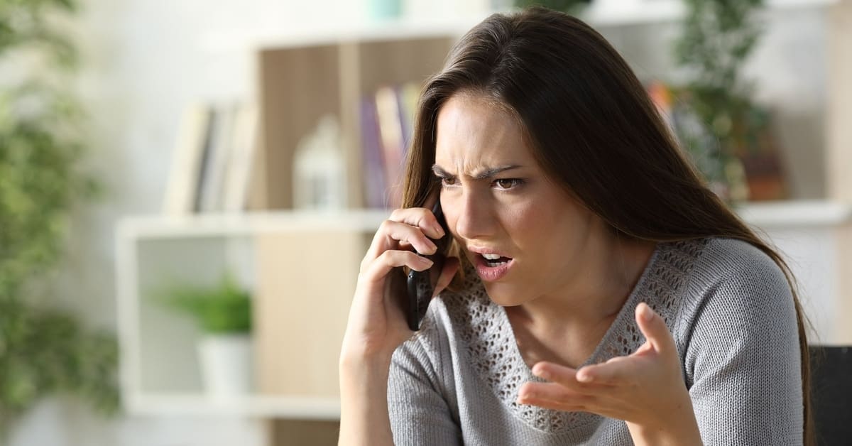 Angry woman calling arguing on smart phone sitting in the living room at home