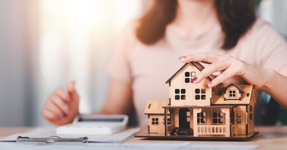 Woman sitting at a desk with hand on small model of a house