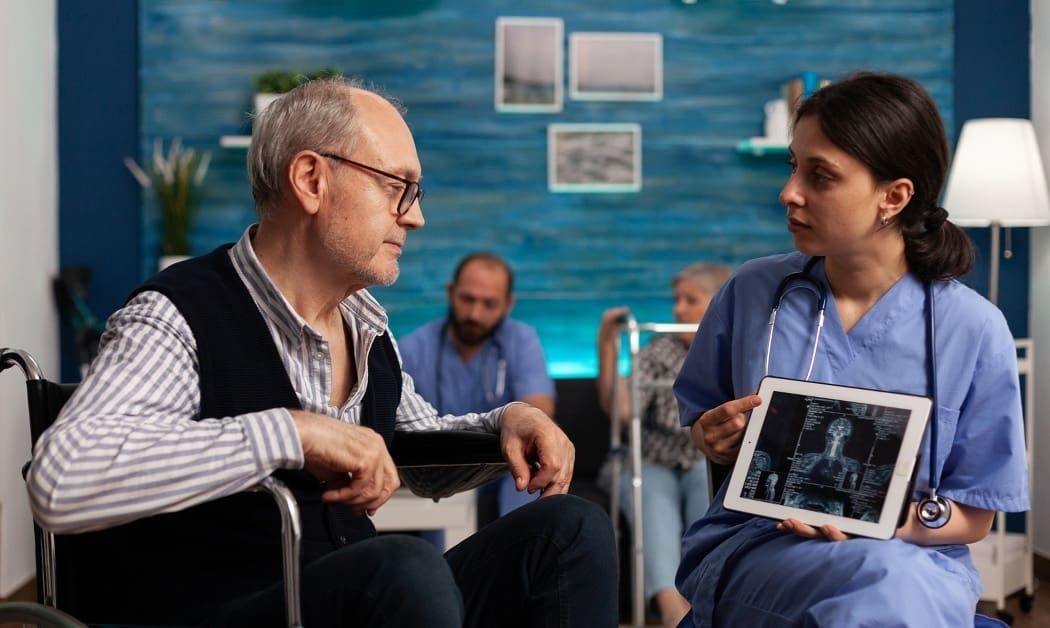 Physical therapy and rehabilitation specialist showing screen with body scan images to elderly patient in wheelchair