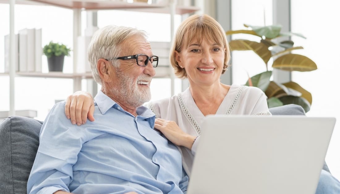 Man and woman using laptop computer on sofa at home together.