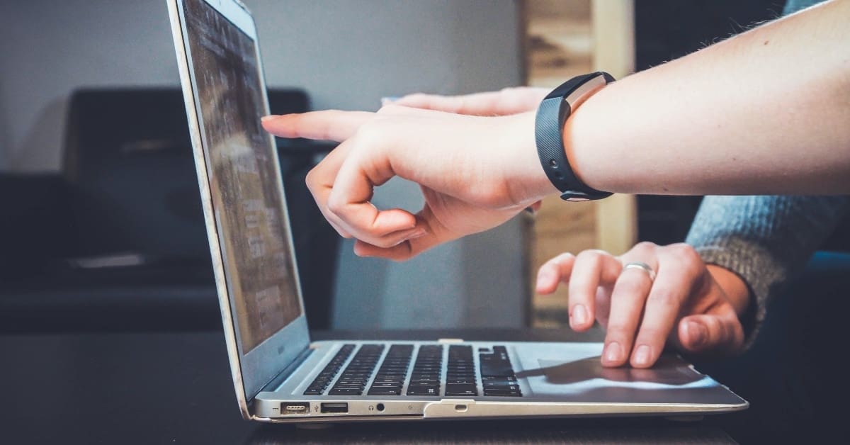 person wearing a watch pointing to laptop screen