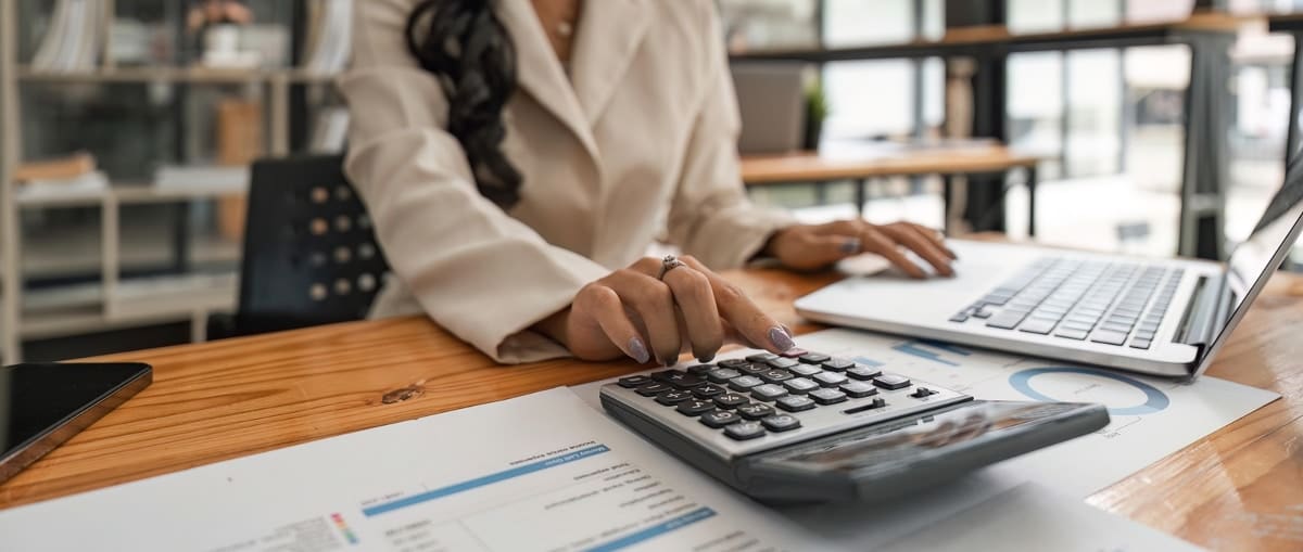 Close-up of businesswoman hands using a calculator to check company finances and earnings and budget. Business woman calculating monthly expenses, managing budget, papers, loan documents, invoices