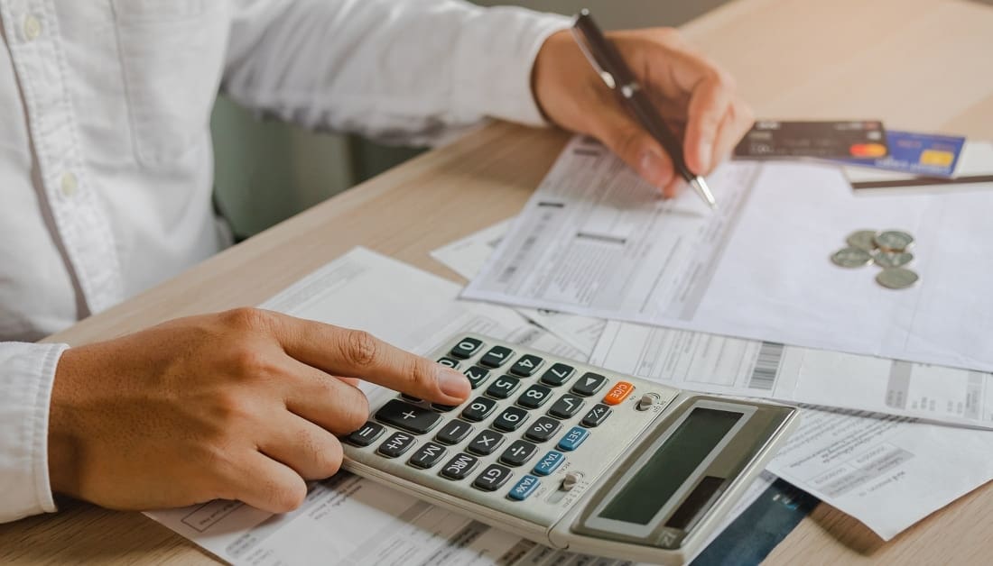 Close up of hand of man holding a pen and using a calculator on a desk while writing on papers or forms