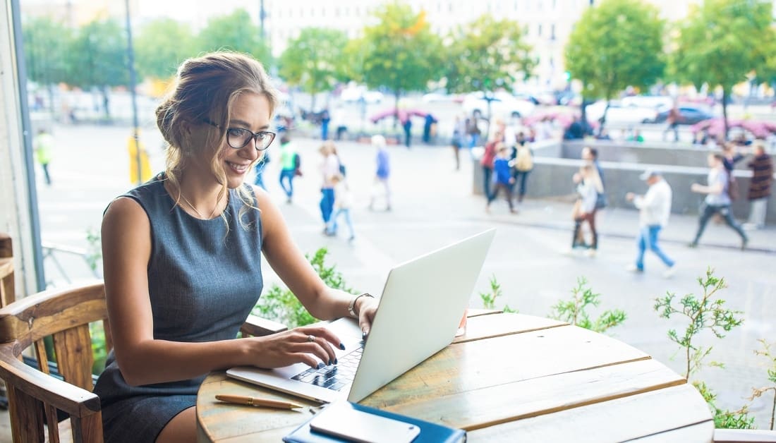 Smiling joyful woman in glasses smart government worker online working on laptop computer while sitting in restaurant during coffee break