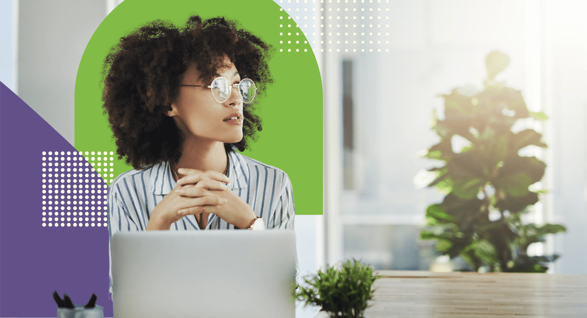 woman with curly dark hair, wearing glasses, looking thoughtful with laptop in front of her