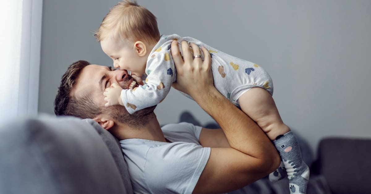 Man holding baby while sitting on couch smiling