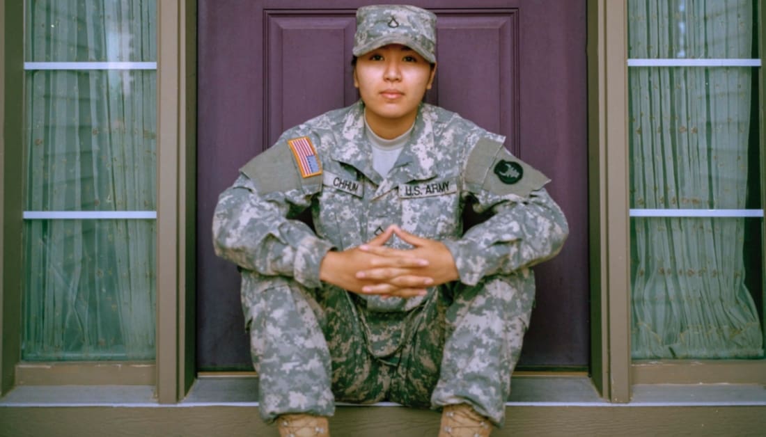 Woman in military uniform sitting on front steps in front of a dark red door