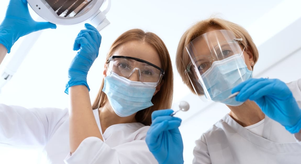 two female dentists wearing masks looking down at a patient in a dental office