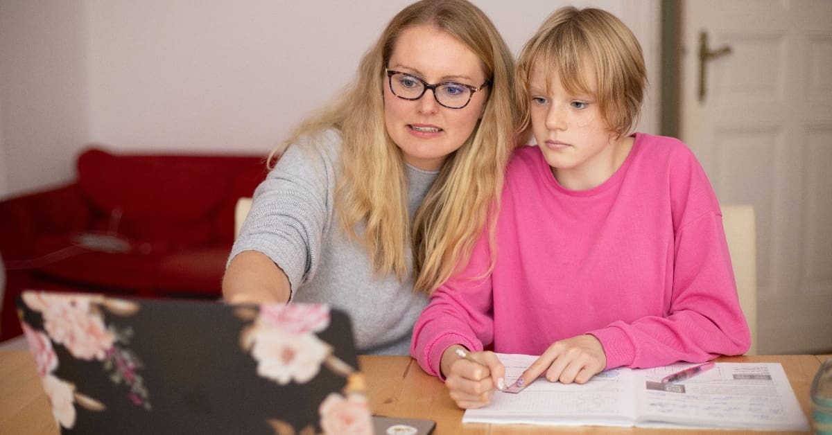 Young girl in pink sweater sitting at a table beside her mom in gray sweater