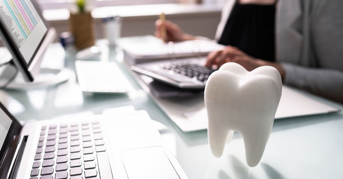 Large figurine of a tooth sitting on a desk with dentist in the background typing on a calculator